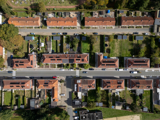 Luchtfoto recht van boven op de wijk met sociale woningen in Wetteren, met rijen huizen met rode pannendaken en zonnepanelen, smalle achtertuinen en straten ertussen