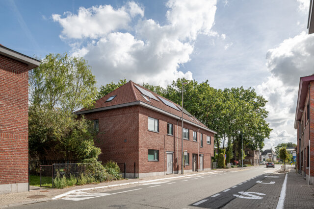 Straat in Wetteren met aan beide kanten sociale woningen in rode baksteen en pannendaken, onder een blauwe lucht met witte wolken