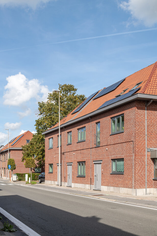Straatbeeld met de sociale woningen in Wetteren, een rij in rode baksteen met een pannendak en zonnepanelen langs de weg
