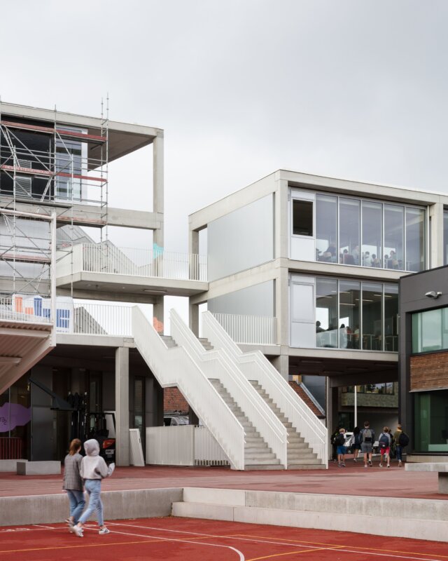gebouw met betonnen buitentrappen en glazen gevel op een rode speelplaats